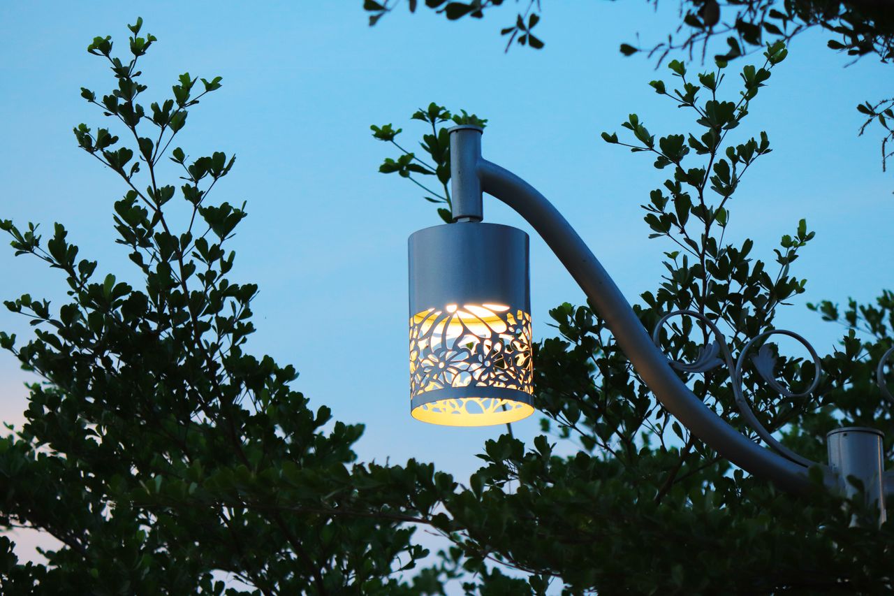 Elegant street lamp glowing against a backdrop of lush green leaves at dusk.